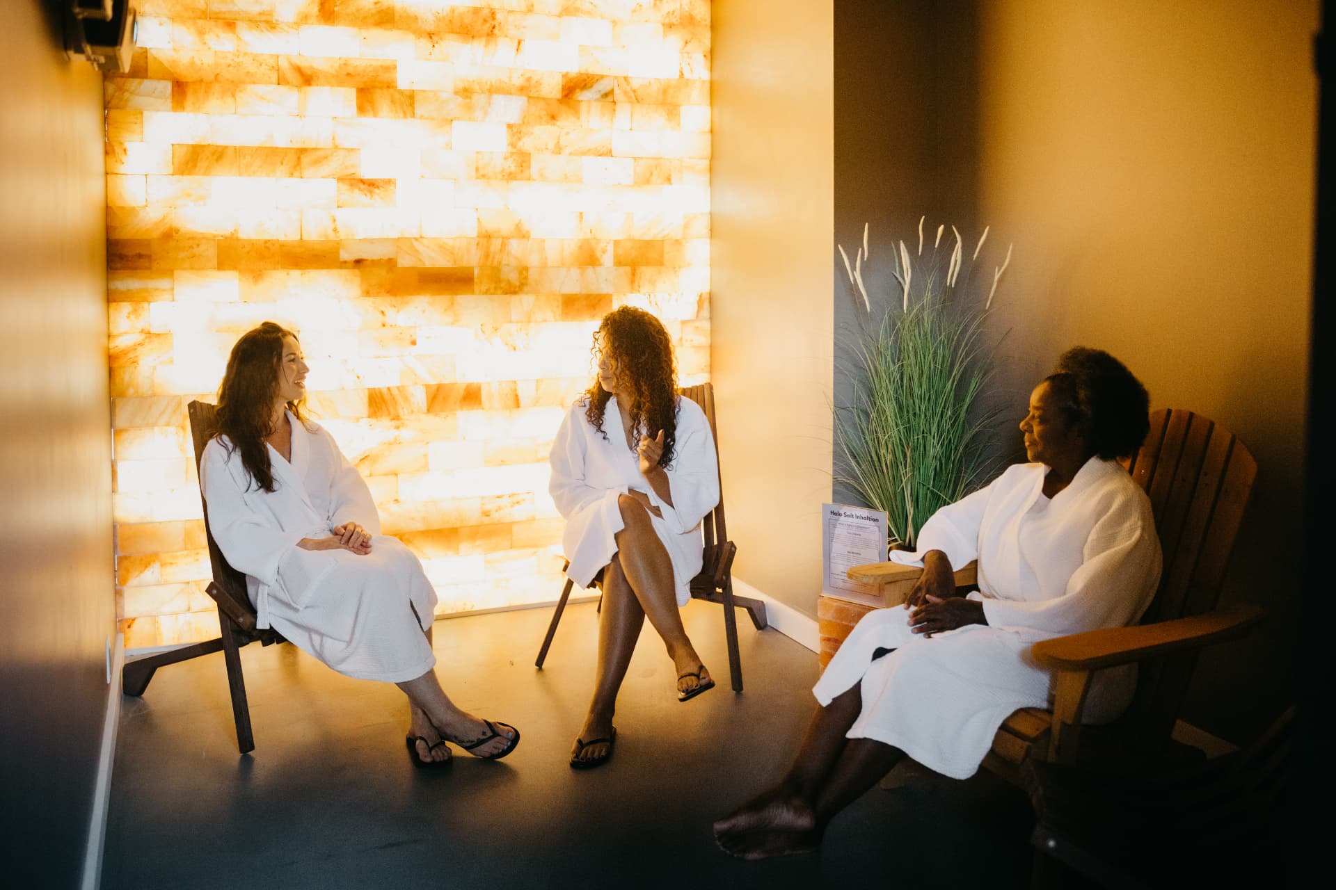 Three members in robes relaxing in front of the backlit Himalayan salt wall at Recharge