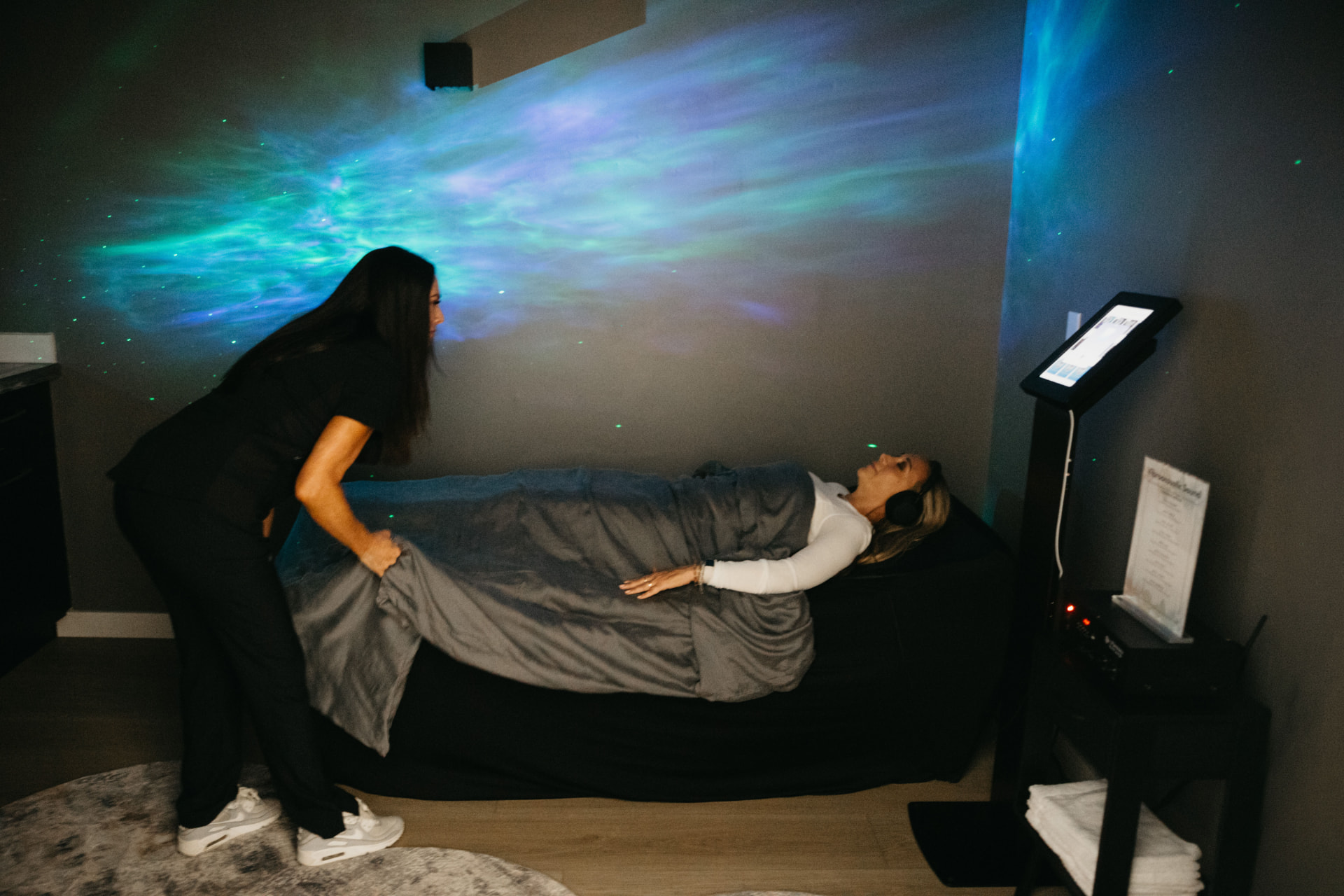 A staff member settling a client onto the vibroacoustic sound bed under a lightscape projection